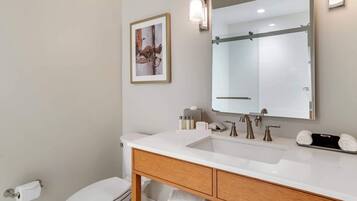 Un baño con lavamanos blanco, tocador de madera, un espejo grande y un cuadro en la pared.