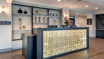 A hotel reception area with a modern design, featuring a reception desk with a patterned back panel, shelves with decorative items, and a sign indicating the hotel is a smoke-free facility.