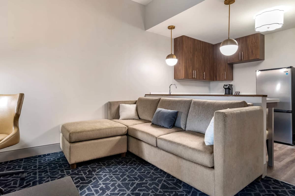 A modern living room with a beige sectional sofa, a small ottoman, and a patterned rug.