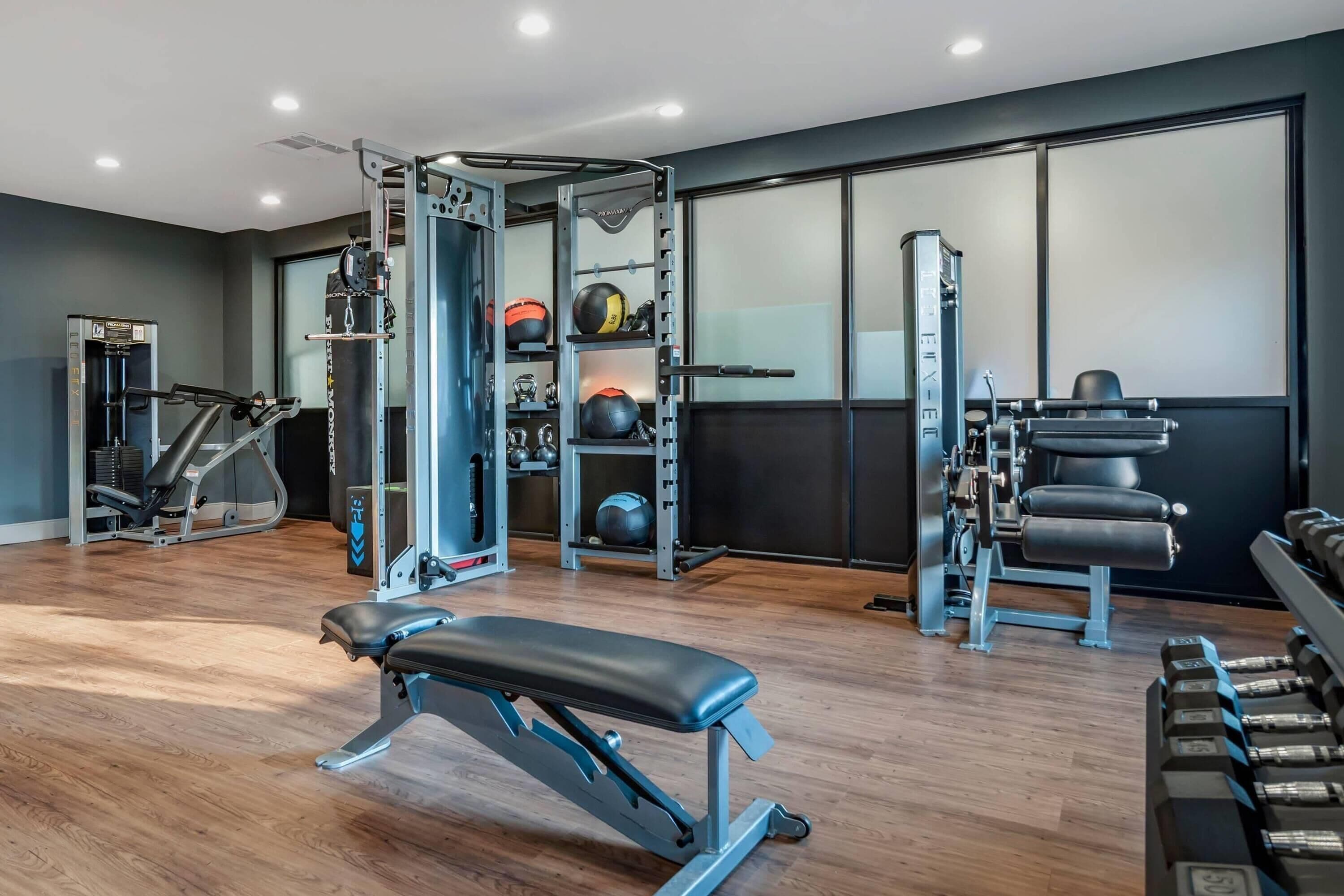 Un gimnasio con bancos, estantes para pesas y varias máquinas de ejercicio.