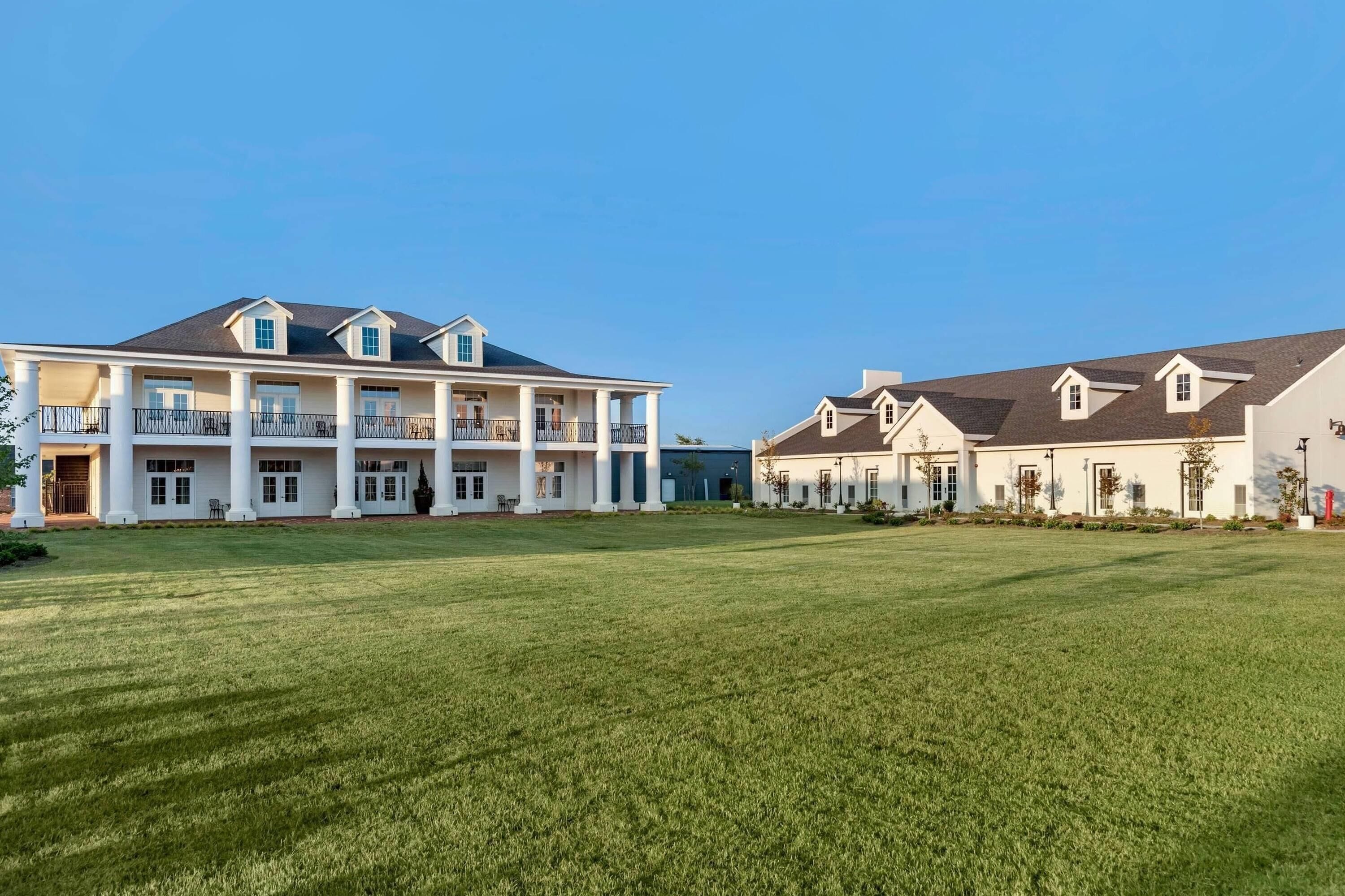 A large, white building with multiple balconies and a spacious lawn.