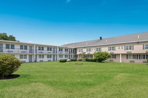 A multi-story hotel with a courtyard featuring a lawn, small trees, and a circular water feature. - Econo Lodge Auburn I-95 (Auburn)