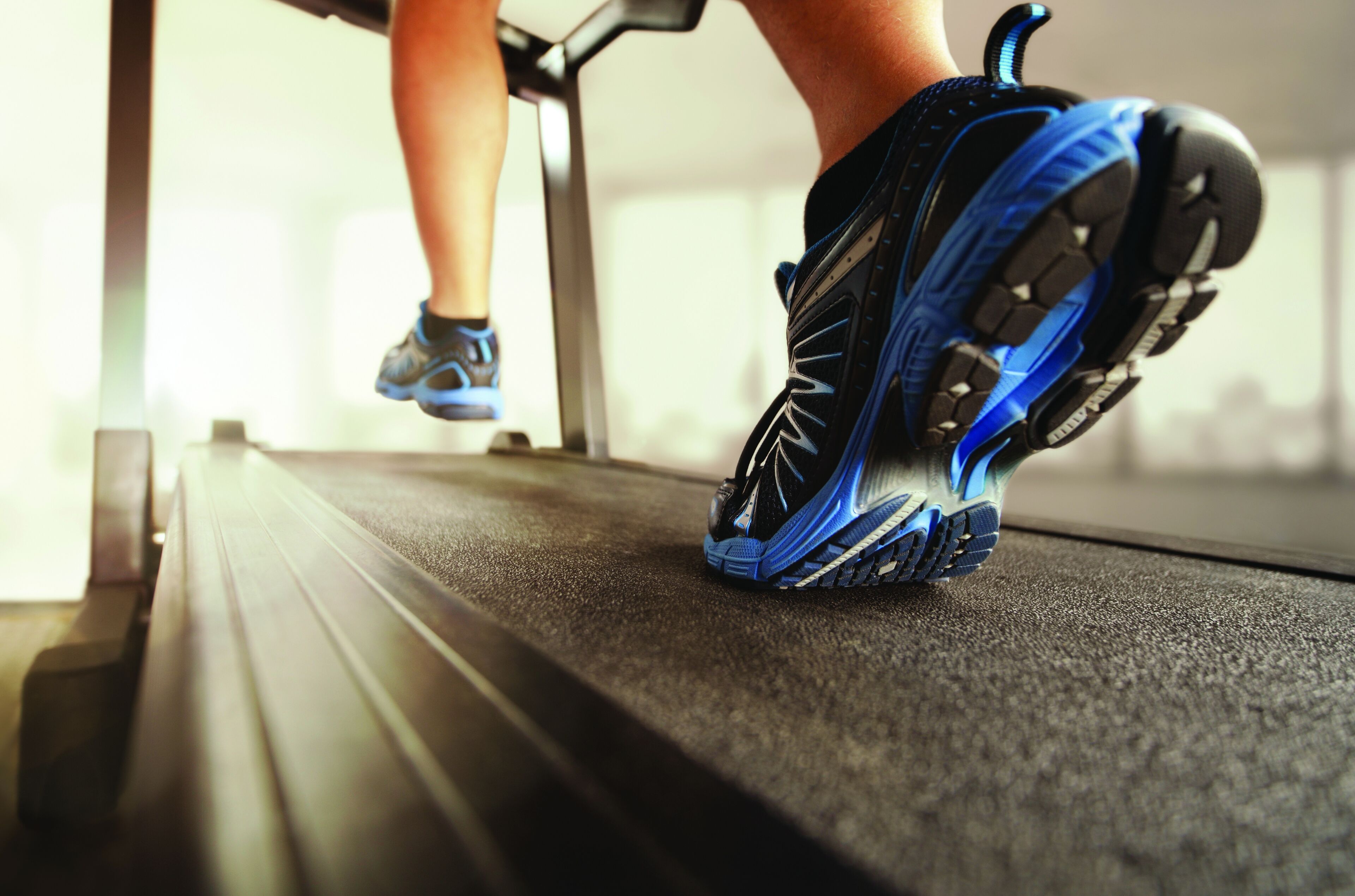 A close-up of a person's foot wearing a blue and black running shoe on a treadmill.