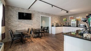 A modern kitchen with a stone wall, a flat-screen TV, and a dining area with a table and chairs. - Econo Lodge Auburn I-95 (Auburn)