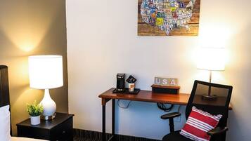 A hotel room with a bed, a desk, a chair, a map artwork on the wall, and a lamp on the nightstand.