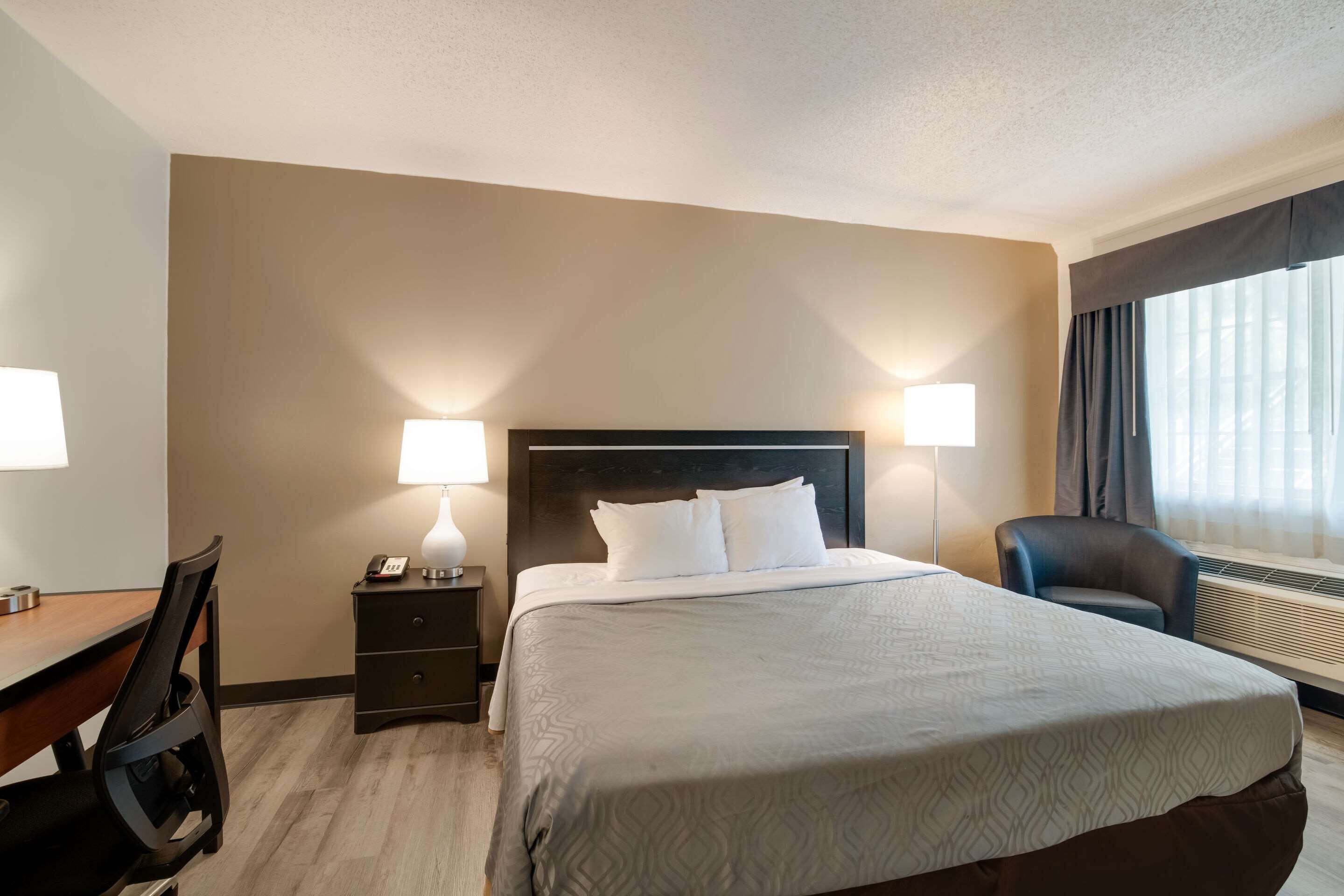 Une chambre d’hôtel avec un grand lit, des lampes de chevet, un bureau avec une chaise et une fenêtre avec des rideaux.