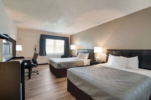 A hotel room with two beds, a desk, a chair, and a television.