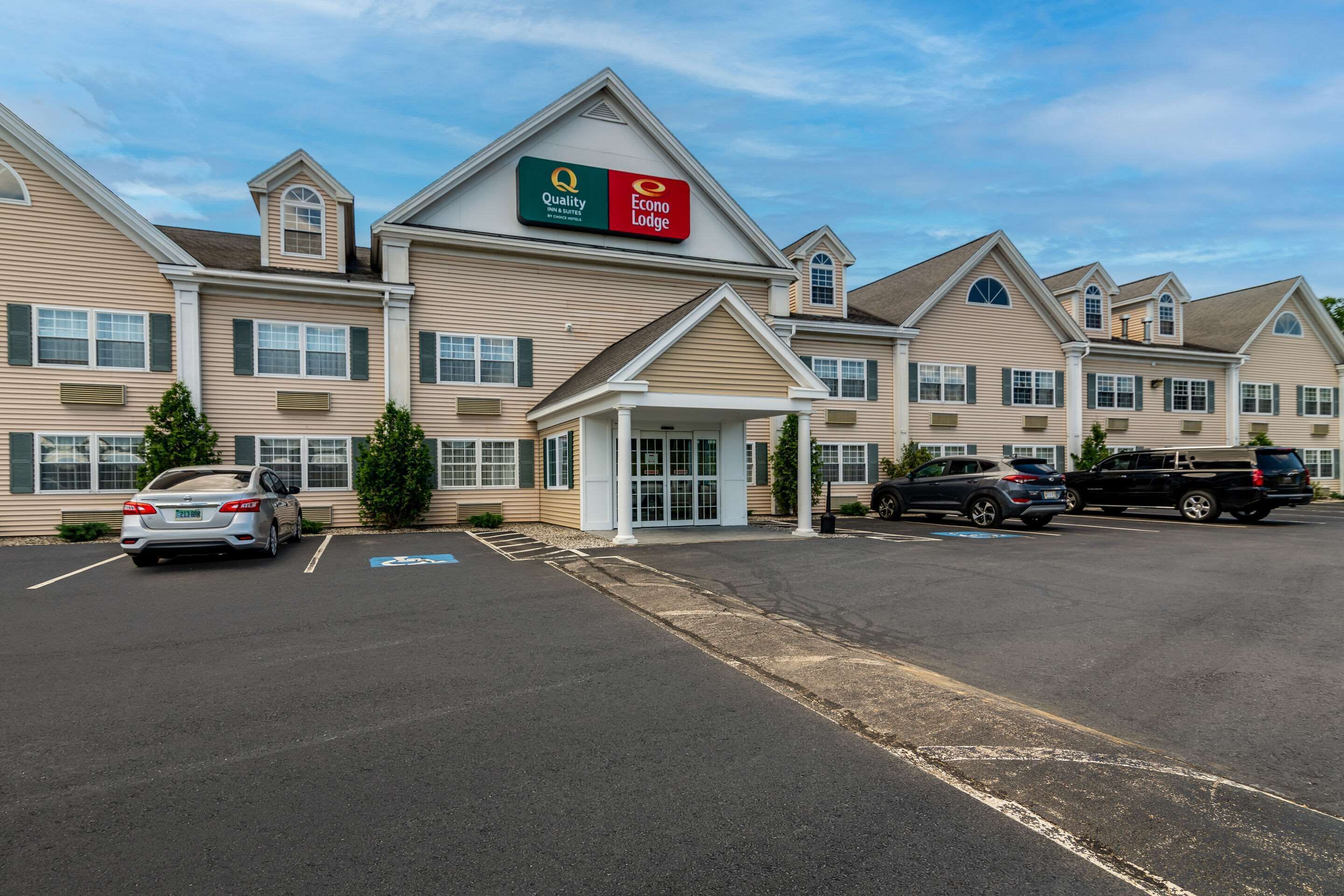 A hotel with a central entrance, multiple parking spaces, and a clear sky.