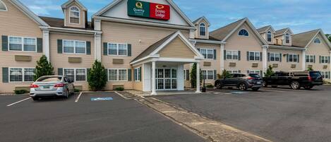 A hotel with a central entrance, multiple parking spaces, and a clear sky.