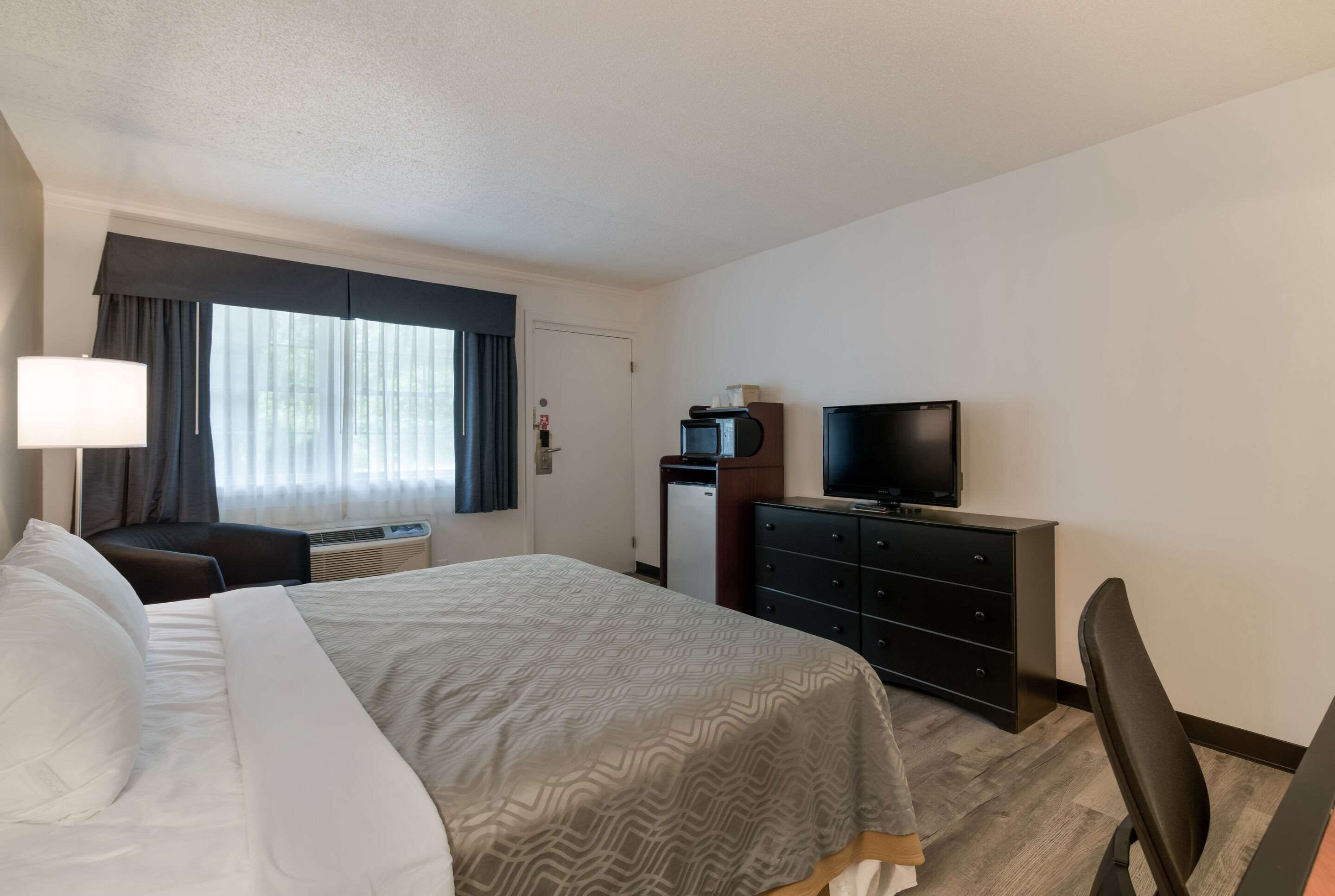 A hotel room with a bed, a desk, a television, a dresser, and a window with curtains.