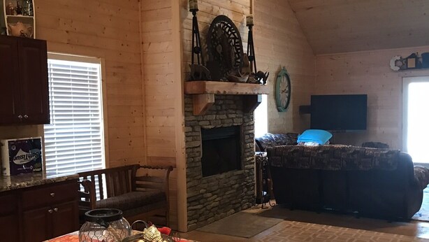 Una sala de estar acogedora con chimenea de piedra, techo de madera y un amplio ventanal.