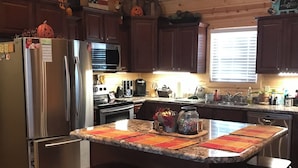 Una cocina con una isla central, taburetes de bar, refrigerador, microondas, horno y varios electrodomésticos.