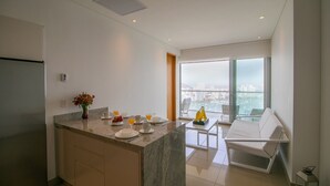 Een moderne keuken met een marmeren eiland, een eetgedeelte met een glazen tafel en witte stoelen, en een balkon met uitzicht op de stad.