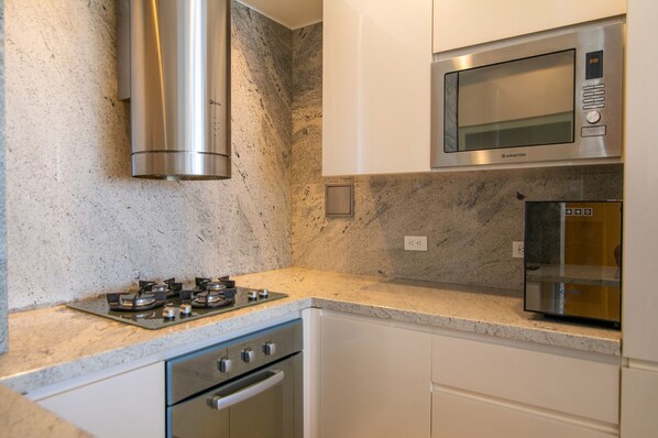 Una cocina con estufa a gas, electrodomésticos de acero inoxidable y muebles blancos.