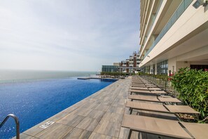 Zona de piscina con vista despejada al océano, terraza de madera y sillones de descanso.
