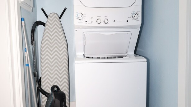 A laundry room with a stacked washer and dryer, a ironing board, and a vacuum cleaner. - Heated Pool, 4 Houses to Beach (Siesta Key)