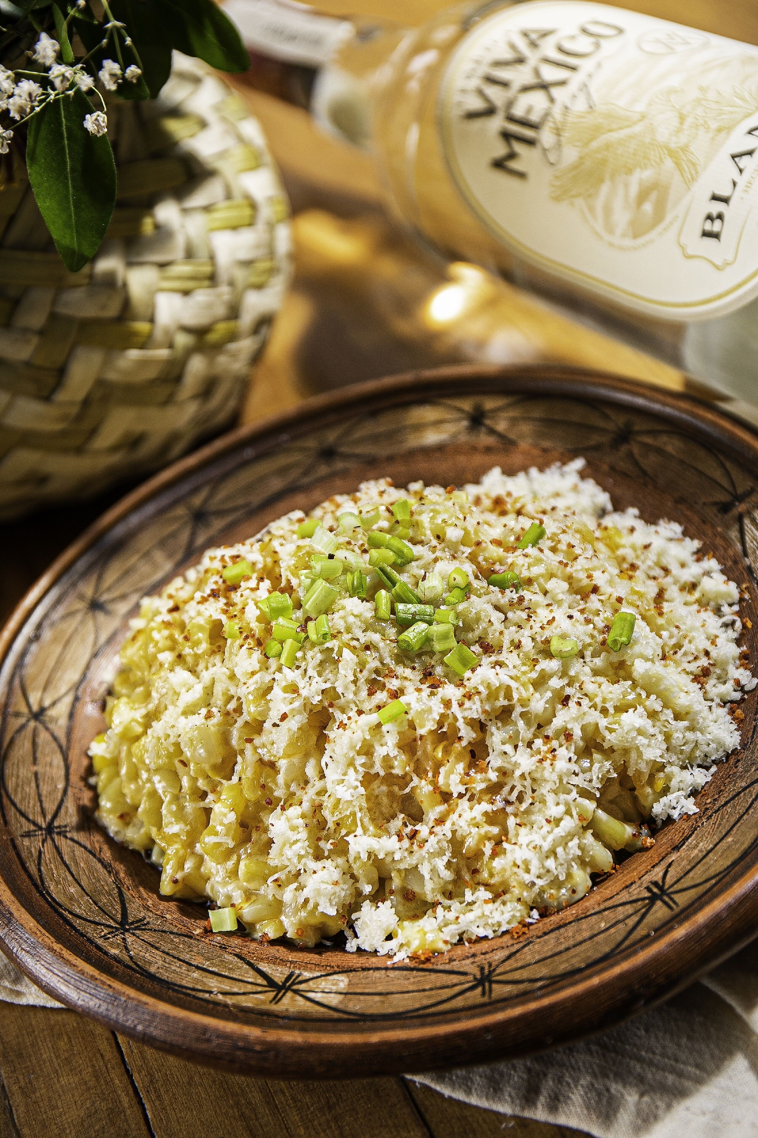 A bowl of rice garnished with green onions and shredded cheese, with a bottle of VIVA MEXICO BLAN in the background.