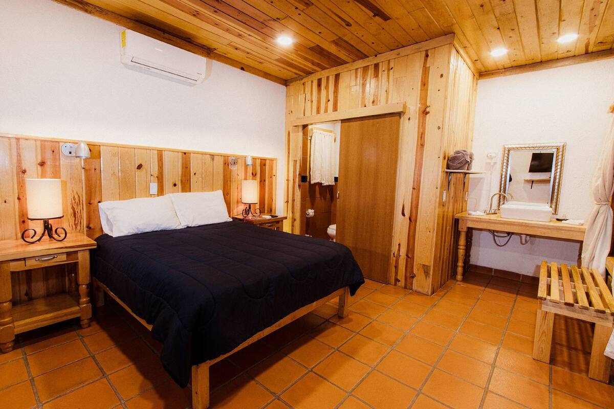 Een houten kamer met een bed, nachtkastjes, een spiegel en een houten bank.
