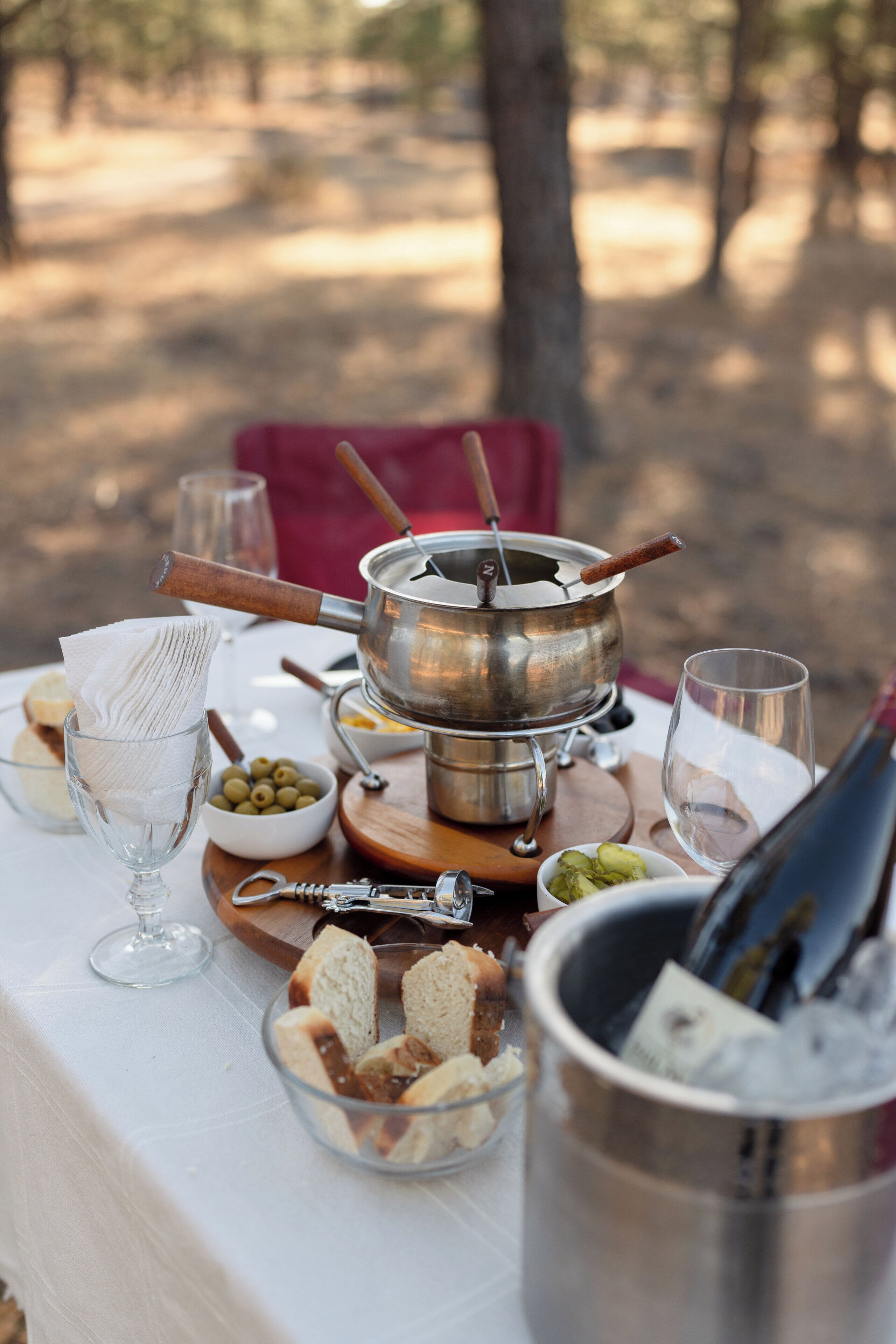 Een picknickopstelling met een draagbaar fornuis, brood, olijven en een fles wijn.