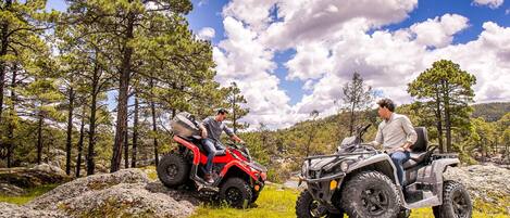 Two people on ATVs in a forested area with rocky terrain and trees.
