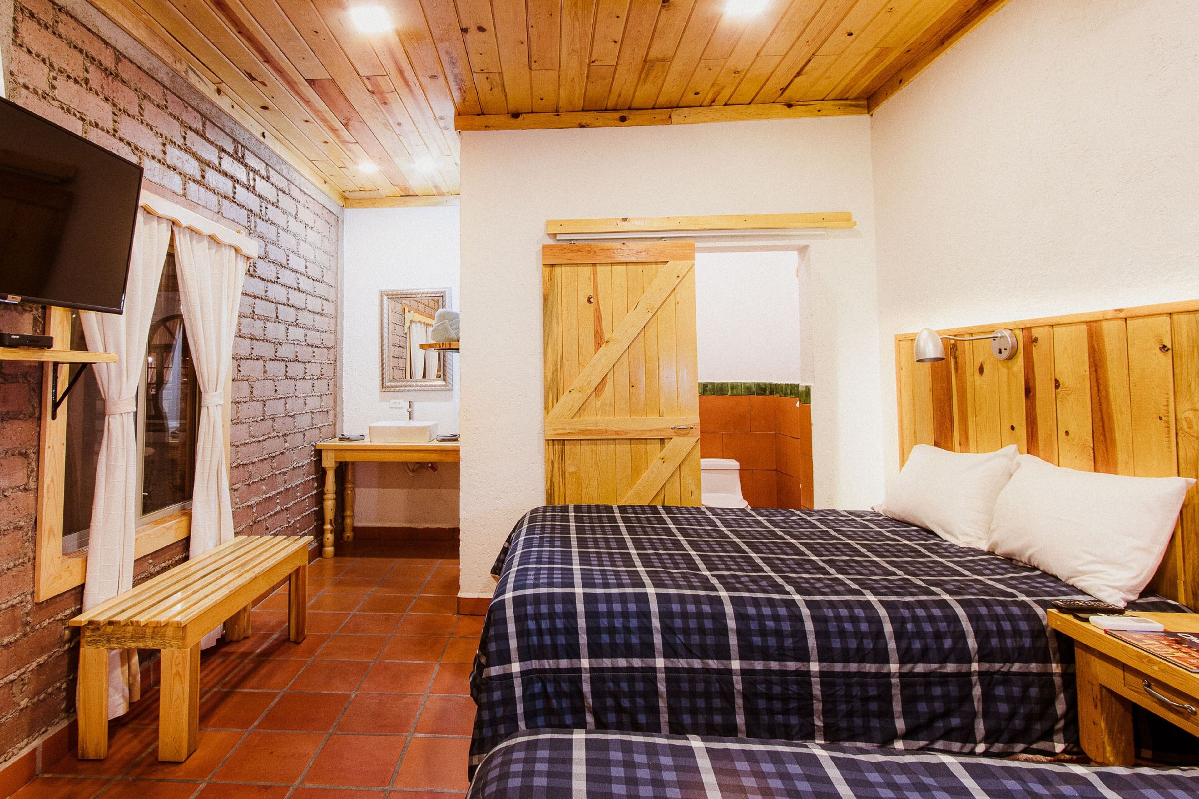 A bedroom with a wooden bed, a bench, a TV, and a wooden door.