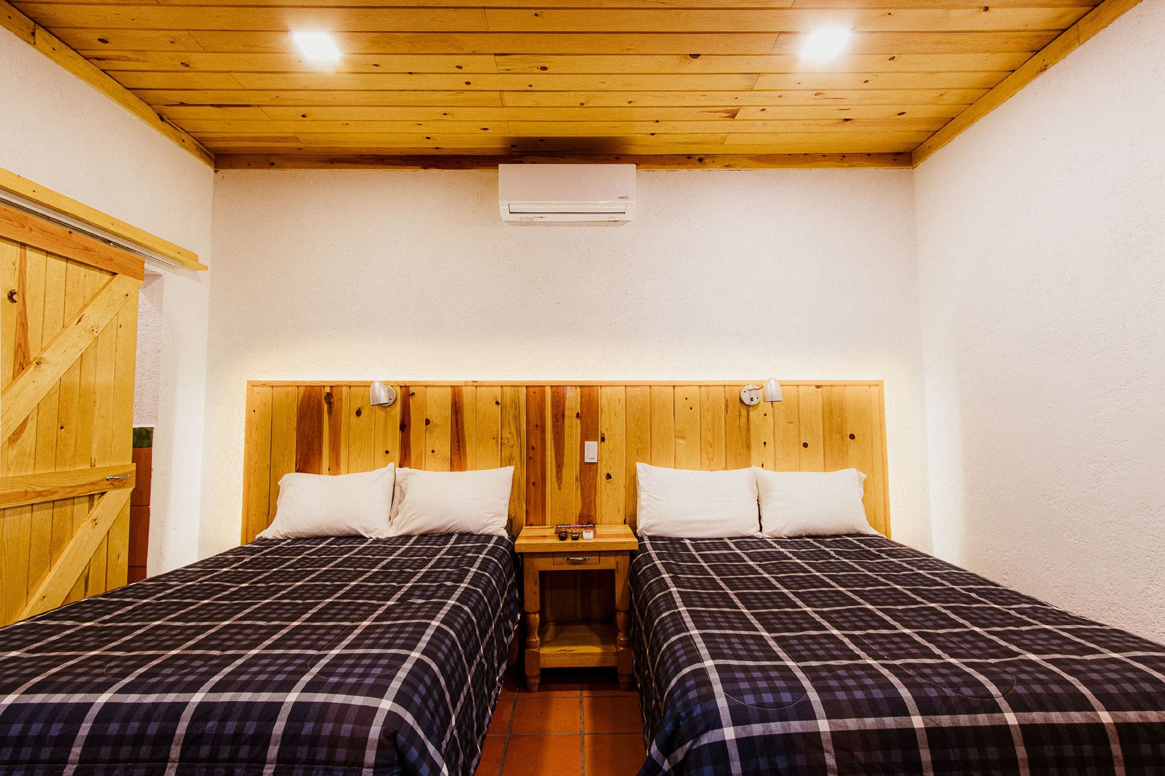A room with two beds, wooden headboard, and a small bedside table with a lamp.