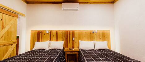 A room with two beds, wooden headboard, and a small bedside table with a lamp.