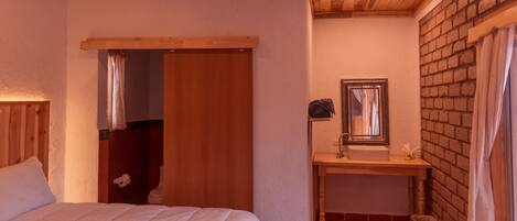 A bedroom with a wooden ceiling, a bed, a wooden door, and a small bathroom with a sink and mirror.