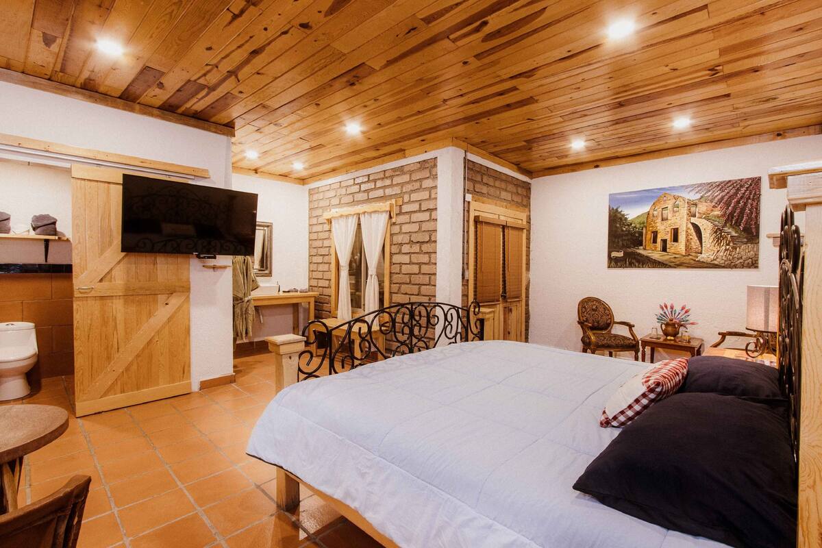 Een slaapkamer met een bed, houten plafond, bakstenen muur en een schilderij.
