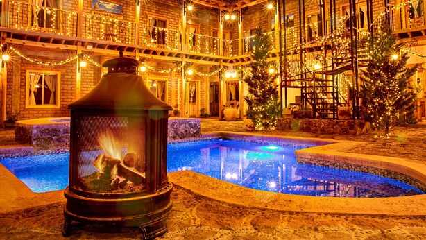 A pool area with a fire pit, surrounded by a building with multiple balconies decorated with lights.