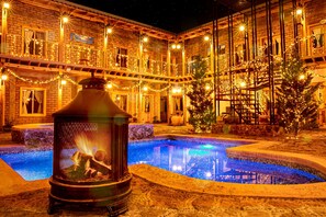Zona de piscina con una chimenea rodeada por un edificio con varios balcones decorados con luces.