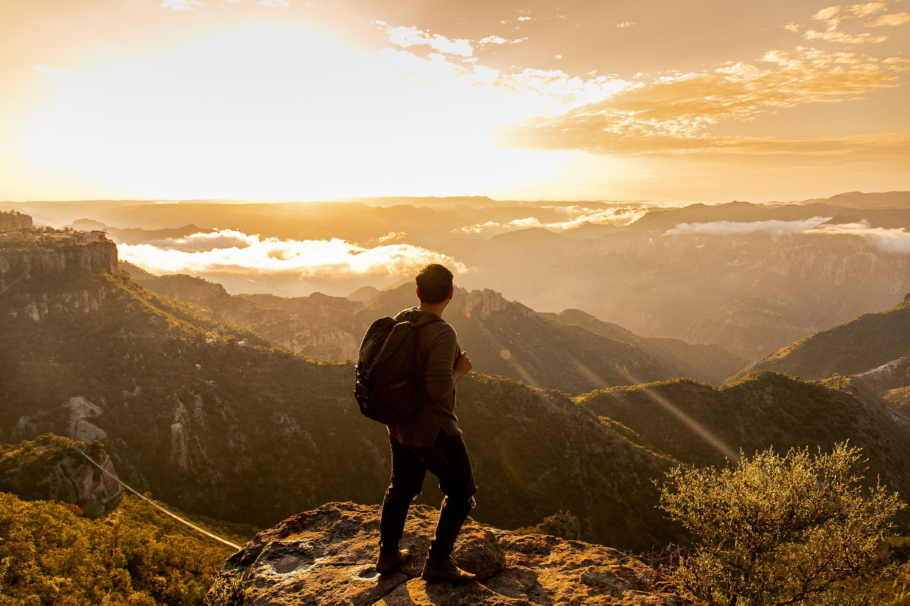 A person standing on a mountain peak overlooking a valley with a clear sky and sunlight.