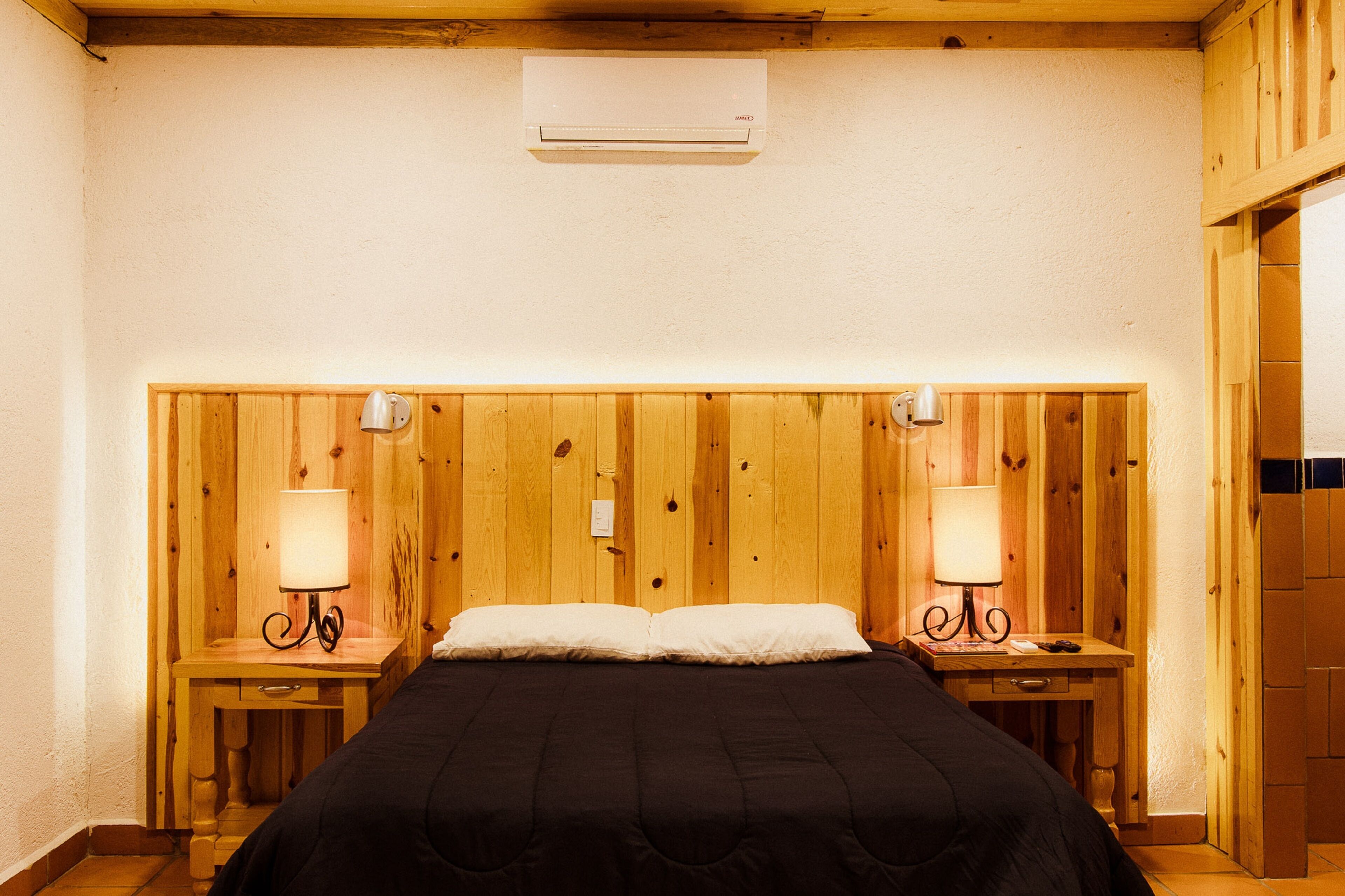 Une chambre à coucher aux murs lambrissés, avec un lit, deux tables de chevet dotées de lampes et un appareil de climatisation fixé au mur.