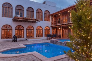 Un área de piscina con un edificio que cuenta con ventanas arqueadas y un balcón con mobiliario exterior.