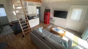 A compact living space with a loft bedroom, kitchenette, and a seating area with a sofa and coffee table. - Cozy cottage loft on the quiet side of Mount Desert Island -Now booking for 2026 (Tremont)