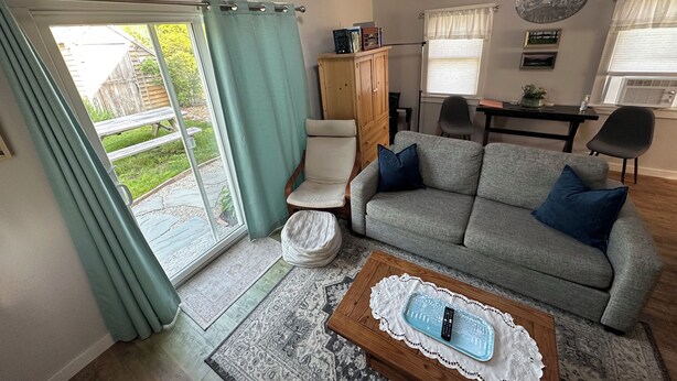 A living room with a grey sofa, a wooden coffee table, and a view of a garden through a sliding glass door. - Cozy cottage loft on the quiet side of Mount Desert Island -Now booking for 2026 (Tremont)