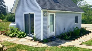 A small, single-story house with a sloped roof, a front door, and a garage door. - Cozy cottage loft on the quiet side of Mount Desert Island -Now booking for 2026 (Tremont)
