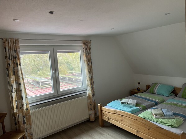 Ein Schlafzimmer mit einem hölzernen Bett, einem Heizkörper, einem Fenster mit Vorhängen und Blick ins Freie.