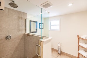 A modern bathroom with a glass-enclosed shower, a wooden shelf with towels, and a small window providing natural light. - Heated Pool, 4 Houses to Beach (Siesta Key)