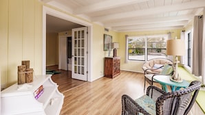 A room with a wooden floor, a white console table, wicker chairs, a small table with a lamp, and a view through a window. - Heated Pool, 4 Houses to Beach (Siesta Key)