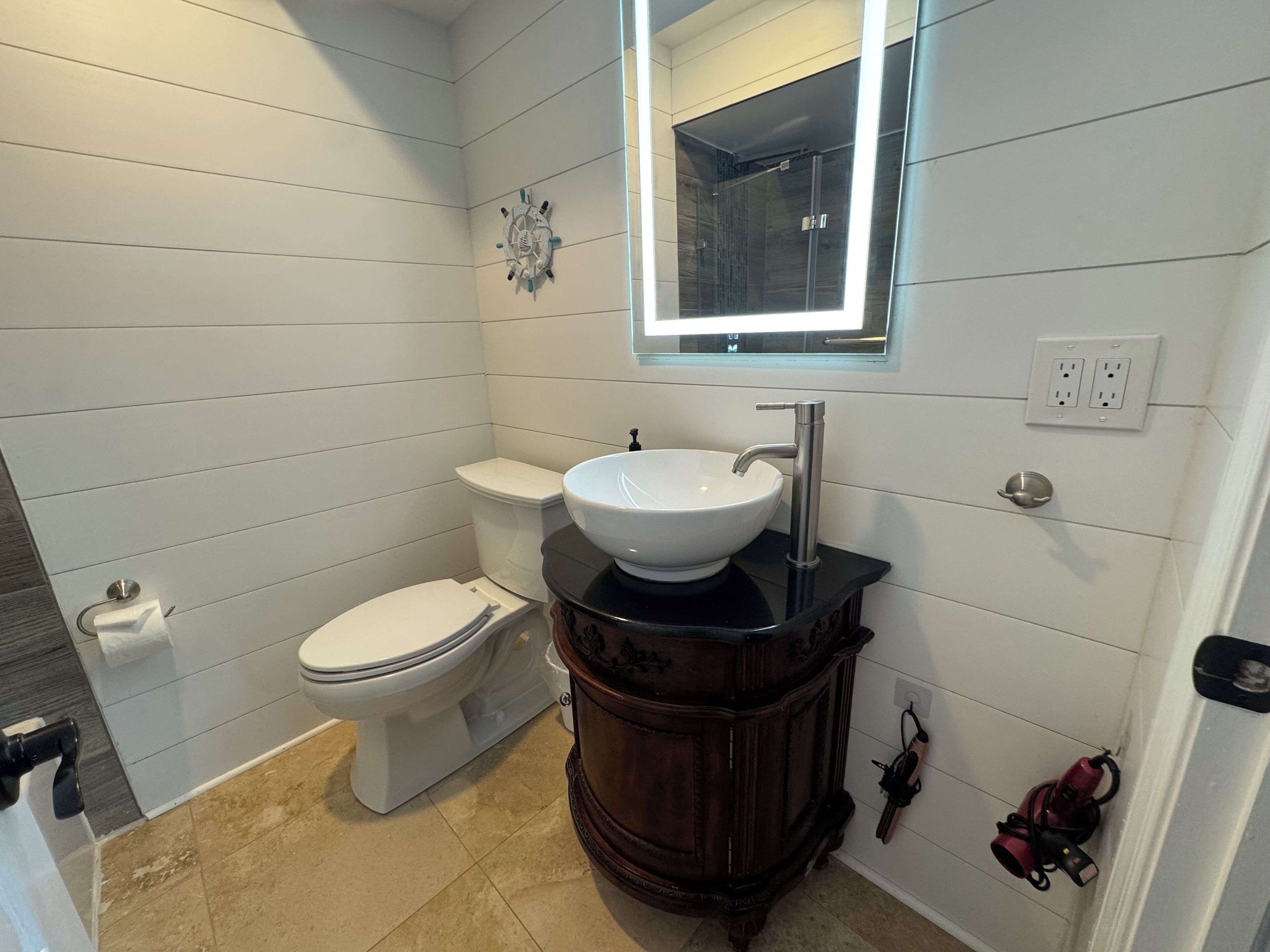 A bathroom with a white toilet, a white sink with a black countertop, and a wooden vanity.