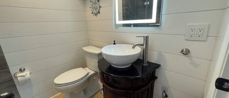 A bathroom with a white toilet, a white sink with a black countertop, and a wooden vanity.