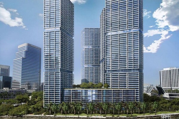 Um edifício moderno e alto com fachada de vidro, rodeado por palmeiras e outros edifícios.