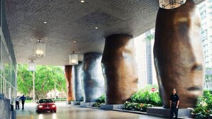 Un bâtiment moderne, orné de grandes sculptures abstraites, et une voiture rouge garée sur le trottoir.