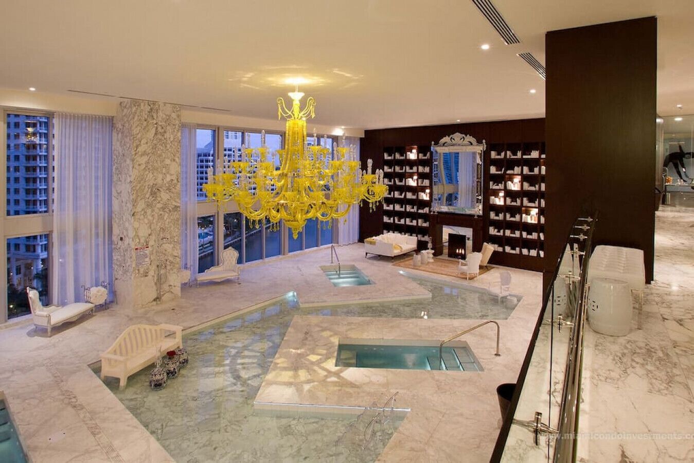 A luxurious indoor pool area with a large chandelier, seating, and bookshelves.