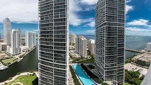 Un immeuble de grande hauteur doté d’une façade moderne en verre, entouré d’autres immeubles de grande hauteur et bordé par une étendue d’eau.