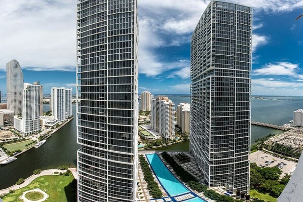 A high-rise building with a modern glass facade, surrounded by other high-rise buildings and a body of water. - Beautiful One Bedroom Condo 16ft ceilings at the W (Miami)