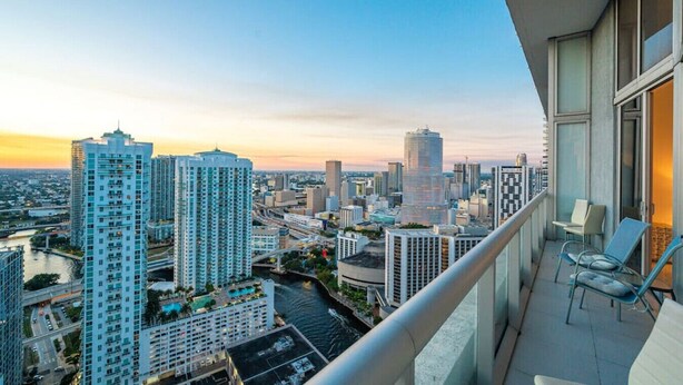 Un immeuble de grande hauteur doté d’un balcon offrant une vue sur le paysage urbain au coucher du soleil.
