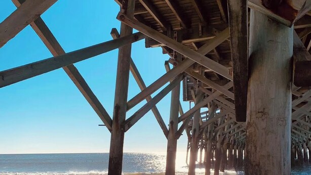 A pier structure with wooden beams and columns extending into the water.