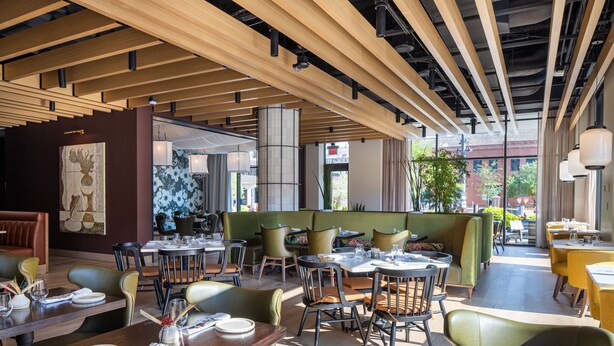 Ein Restaurant mit Holzbalkendecke, grünen Sitzgelegenheiten und Blick auf die Stadt.
